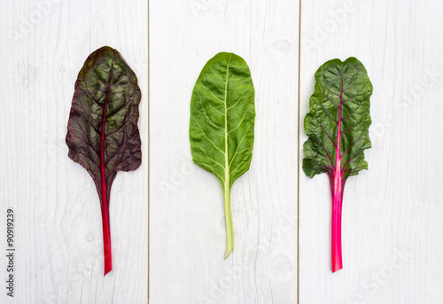 Three leaves of fresh swiss chard on a white table