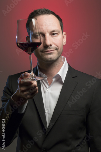 man tasting red wine in jacket in front of red background