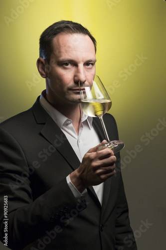 man tasting white wine in jacket in front of yellow background