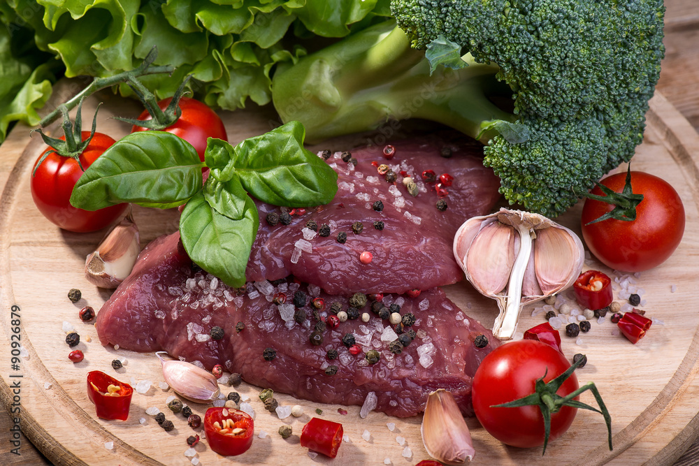 Raw beef steak with spices on a wooden background