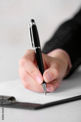 Female hand with pen writing on paper at workplace