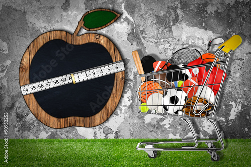 Canvas Print shopping cart with sporting goods on grass in front of stone wall with apple sha