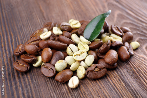 Green and brown coffee beans with leaf on wooden background