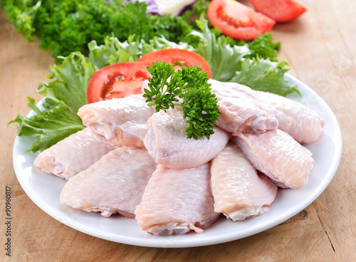 Raw chicken wings with vegetables on wooden board