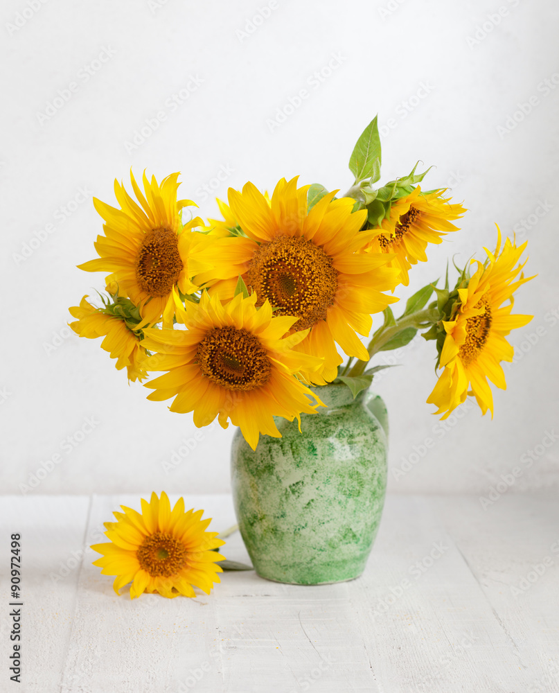 Naklejka premium Bouquet of sunflowers in old ceramic jug on wooden table.