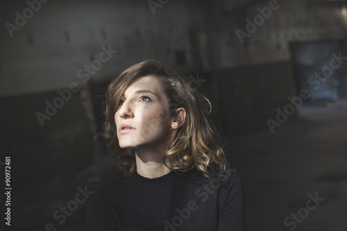 Beautiful woman with a serious expression on her face looking up with a view of abandoned building in the background