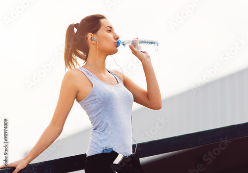 Young woman taking a break from exercising, drinking water 