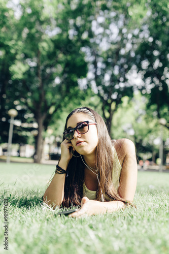 Beautiful young woman lying on the grass in a park with a smart © photopitu