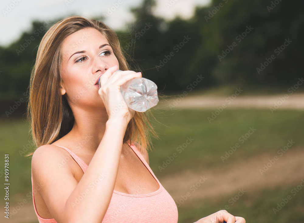 Portrait of young beautiful woman wearing pink t-shirt drinking water at summer green park. Portrait of young beautiful woman wearing pink t-shirt drinking water at summer green park.