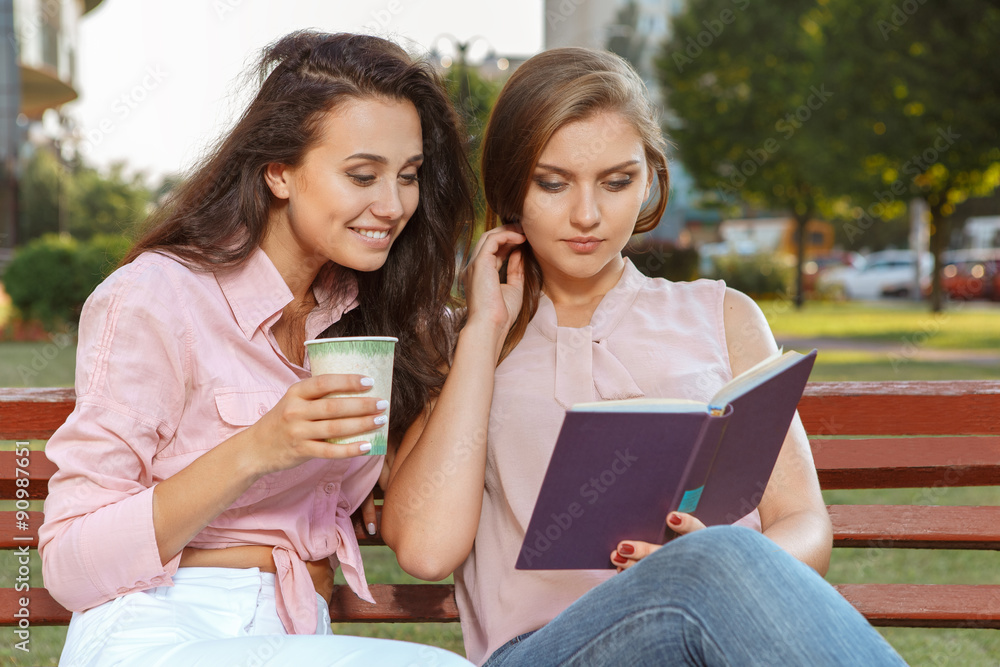 Two girls reading a book on the bench Two girls reading a book on the bench