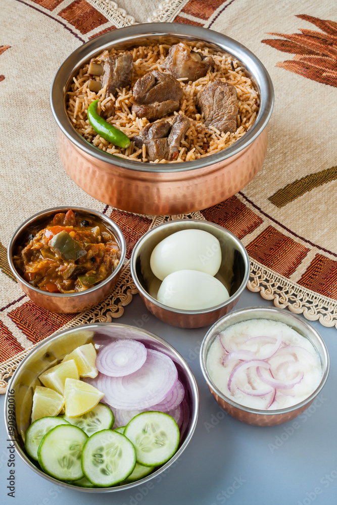 Mutton biryani with traditional sides - Overhead view from the top of delicious mutton (lamb) biryani served in authentic copper utensils with salad (raita), gravy and egg. Natural light used.
