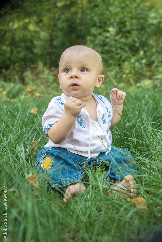 Baby in embroidery on the green grass in the park