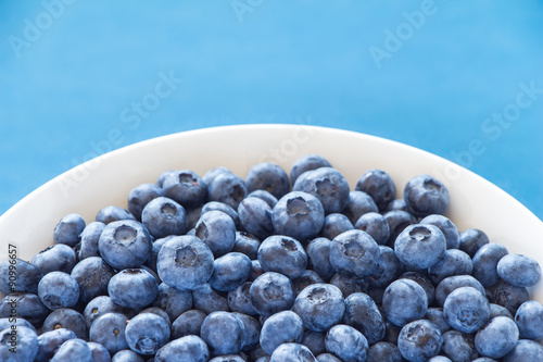 Blueberries in white bowl on colorful blue backround