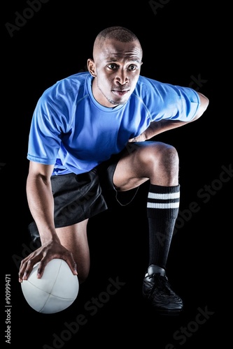 Serious rugby player kneeling while holding ball