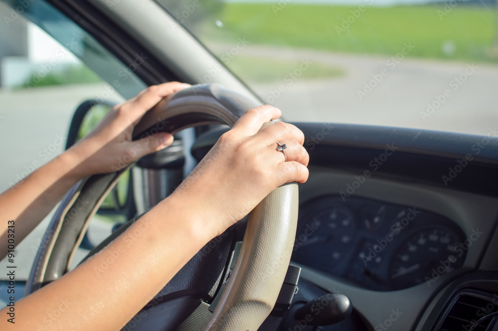 Young woman's hands holding steering wheel inside car in summer