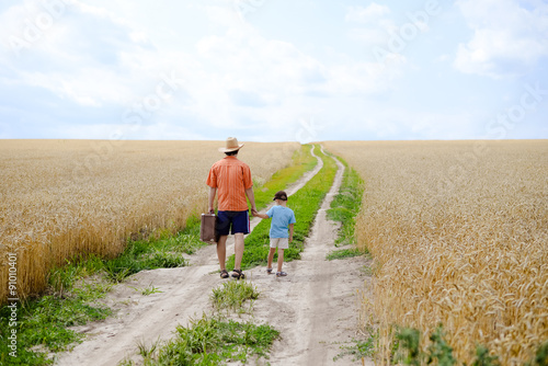 Man with suitcase and boy walking away in wheat field