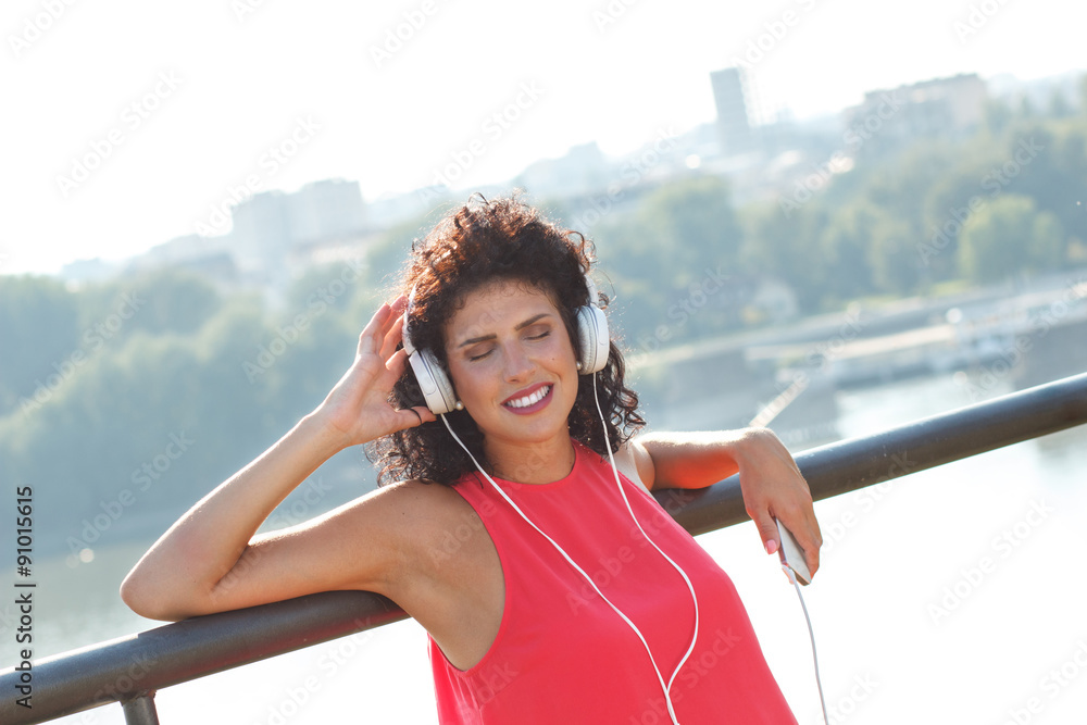 Fototapeta premium Young woman leaning on a fence listening to music on the phone with closed eyes.
