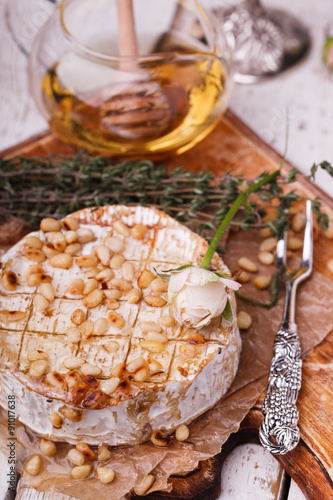Baked Camembert with honey, pine nuts and thyme on an old cutting Board.