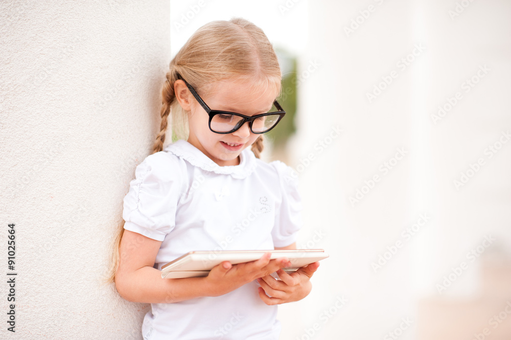 Smiling kid girl playing on tablet outdoors. Touching screen. Childhood. 