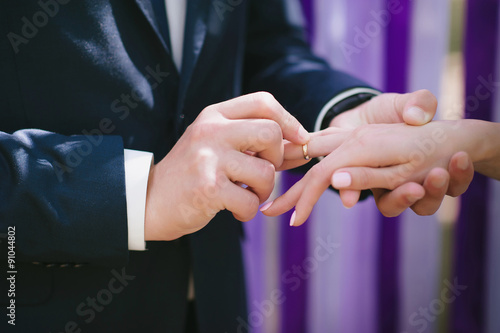 The bride and groom wear each other at a wedding ceremony when rings on a background of multi-colored ribbons, love, marriage, relationships