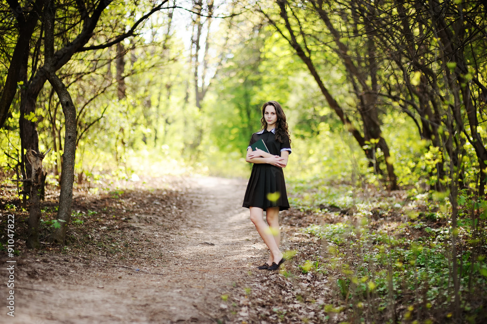 Beautiful schoolgirl with a book in hands on a background of green trees Beautiful schoolgirl with a book in hands on a background of green trees