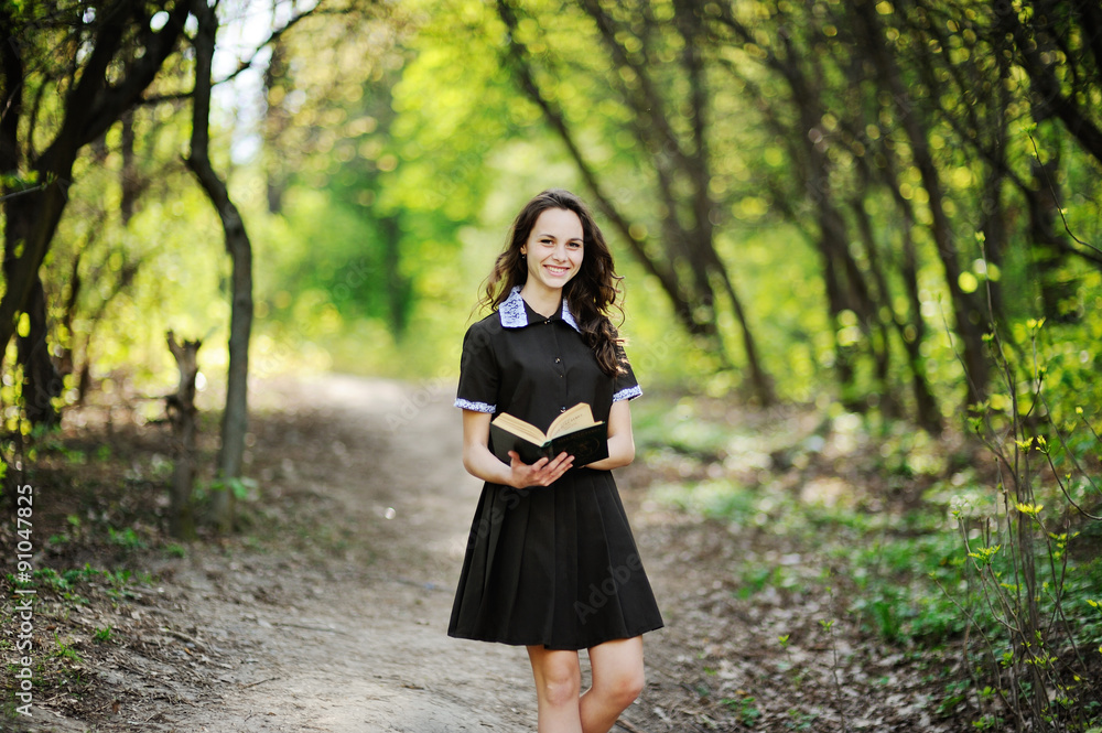 Beautiful schoolgirl with a book in hands on a background of green trees Beautiful schoolgirl with a book in hands on a background of green trees