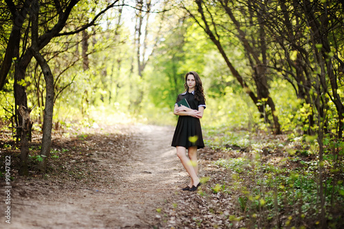 Beautiful schoolgirl with a book in hands on a background of green trees © Evgeniy Kalinovskiy