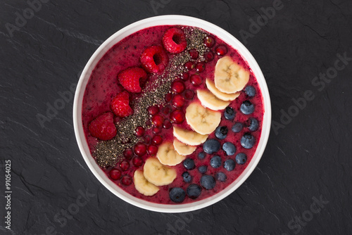 berry smoothie bowl with chia seeds, bananas, blueberries, currant and raspberries on black slate