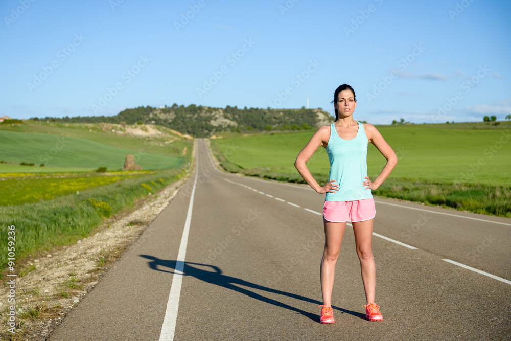 Sporty motivated woman portrait. Female athlete standing outdoor after running and exercising on countryside road.