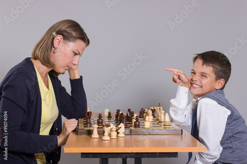 The little boy laughs with her mom playing chess.