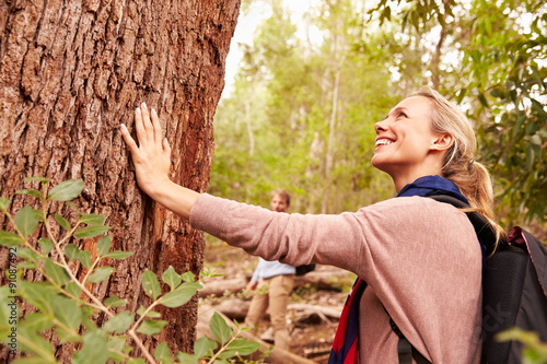 Woman touching a tree in a forest, husband in the background