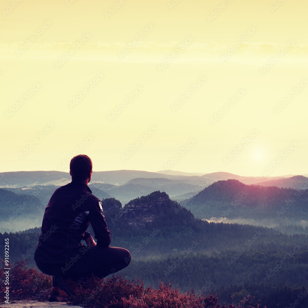 Sunrise sports. Hiker in in dark sportwear in squatting position on a rock in heather bushes, enjoy the scenery Sunrise sports. Hiker in in dark sportwear in squatting position on a rock in heather bushes, enjoy the scenery