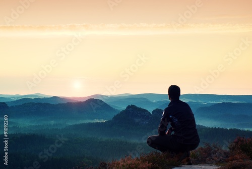 Sunrise sports. Hiker in in dark sportwear in squatting position on a rock in heather bushes, enjoy the scenery