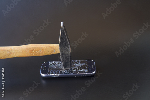 A broken smartphone with a hammer on a dark background