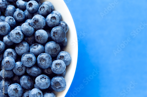 Blueberries in white bowl on colorful blue backround