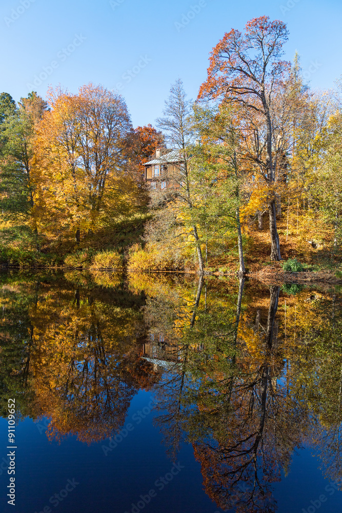 Trees in autumn colors on a lake with a house on a hill reflecting in water