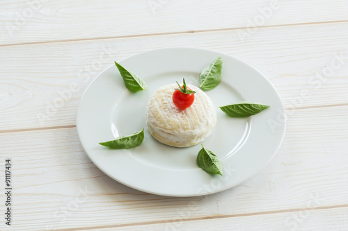 Camembert round cheese with cherry tomatoes and basil on a round white plate.