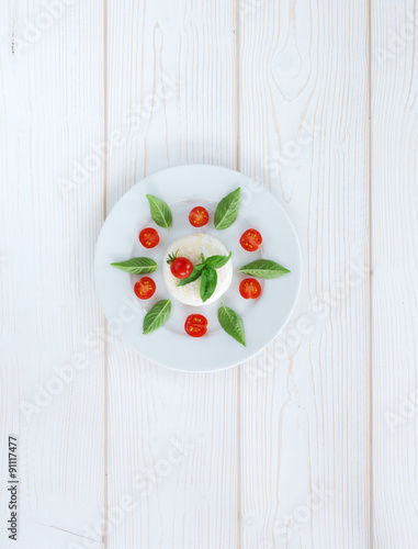 Round camembert cheese with cherry tomatoes and basil on a round white plate. top view
