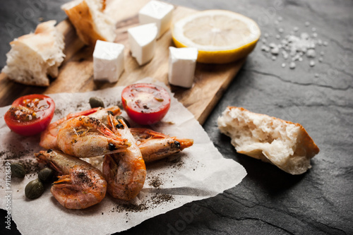 Grilled shrimps on the peace of paper with different snack on the black stone table horizontal