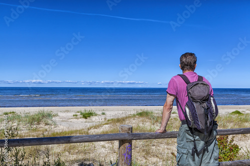 Ein Rucksack-Tourist auf einer Wanderung schaut über den Strand und die Ostsee auf einen strahlend blauen Sommerhimmel © GinaKoch