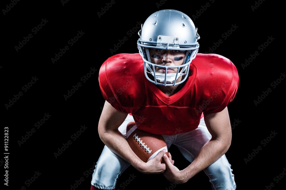Portrait of American football player bending while holding ball