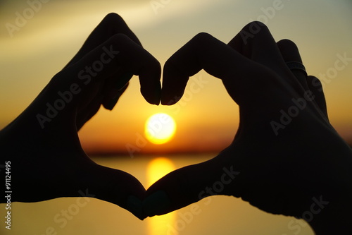 Woman makes heart  hands directs the sunset