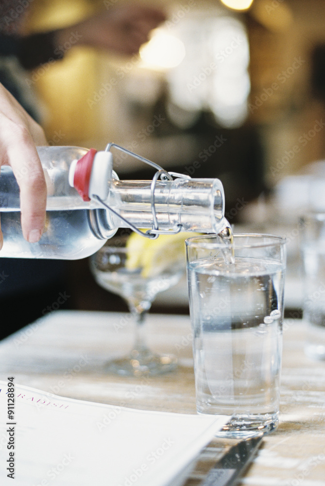 A hand pouring water from a bottle with a clip top into a glass. A hand pouring water from a bottle with a clip top into a glass.