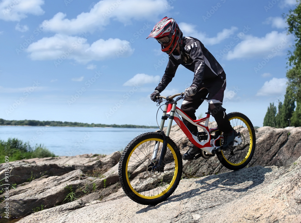 Naklejka premium Sportsman in sportswear on a mountain bike rides on the stones in the extreme style of downhill