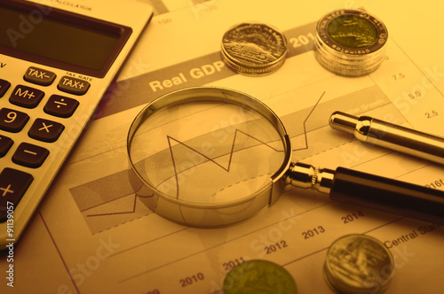 Magnifying glass, calculator, pen, and coin on financial graph