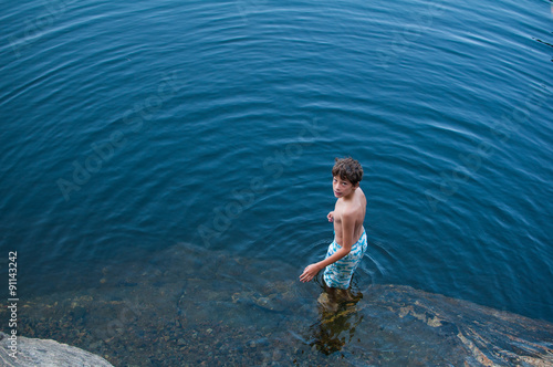 young boy wearing a bathing suit standing in a lake looking up at the camera