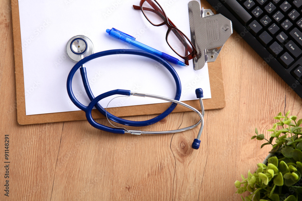 A medical stethoscope near a laptop on a wooden table, on white A medical stethoscope near a laptop on a wooden table, on white