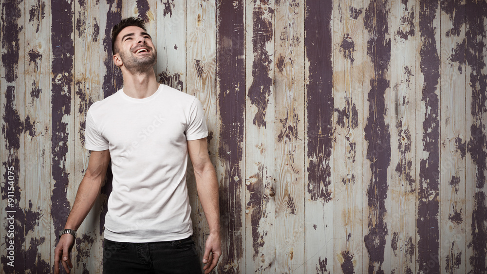 Fototapeta premium Smiling man in blank t-shirt, grunge wooden wall background