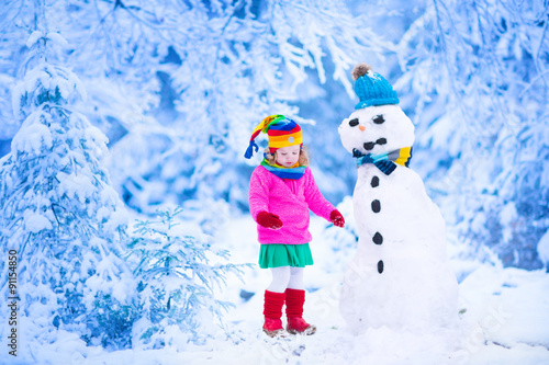 Little girl building a snow man in winter