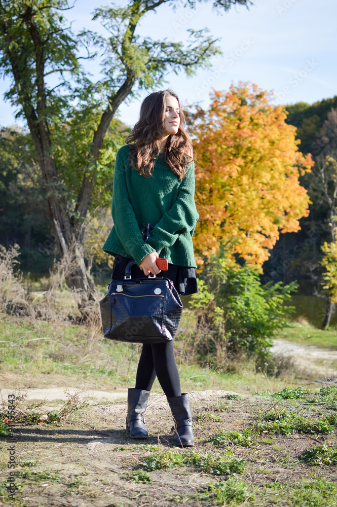 Young woman with black leather handbag standing in autumn